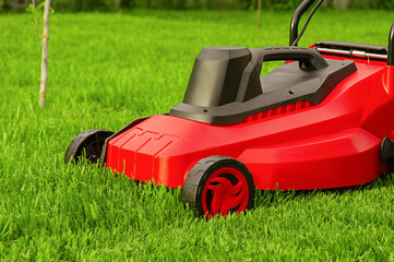 A red and black lawn mower stands on the grass.