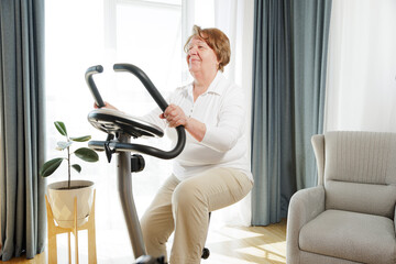 Senior woman training at home on a bicycle trainer, healthy lifestyle after retirement