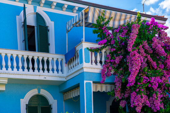 Blue Mediterranean villa with balcony, shutters, and pink bougainvillea flowers