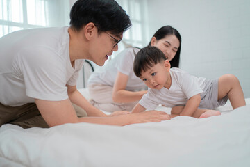 Fototapeta premium Asian family moment at home, smiling mother holding toddler boy who reaches out to father with curiosity and joy. Concept of parenting, bonding, love, and early childhood development.