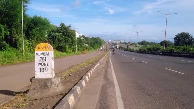 NH-48 milestone shows 251km to Mumbai, 100km to Pune; a motorcyclist, green foliage, and hills under a sky. Pune-Bengaluru Expressway, a new greenfield route, supplement NH-48 and connect two cities.