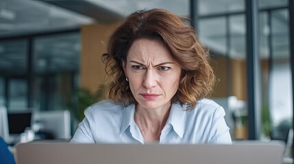 Woman frowning at laptop screen in office. Professional grappling with problem. Frustration and concentration in business.