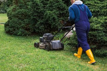 Fototapeta premium The concept of gardening and country life. A lawn mower man mows the grass in the backyard. Agricultural machinery for garden maintenance. The banner.