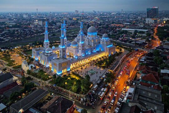 Aerial view of a luminous Sheikh Zayed Grand Mosque bathed in ethereal blue light contrasts against the urban tapestry, Surakarta, Central Java, Indonesia.