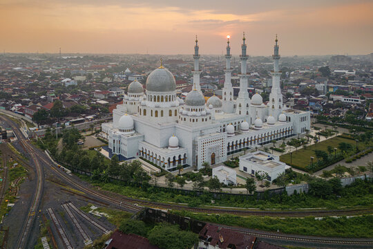 Aerial view of the grand mosque with its towering minarets and gleaming white facade, a serene contrast against the urban sprawl, Solo, Central Java, Indonesia.