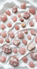 A variety of polished and raw rose quartz crystals arranged artfully on a smooth white fabric.