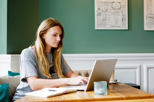 Portrait of young woman using technology of smartphone and looking at laptop. Young woman freelancer using laptop computer working in restaurant or hipster indoor cafe with coffee.