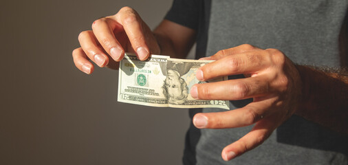 Caucasian man showing torn dollar banknote.