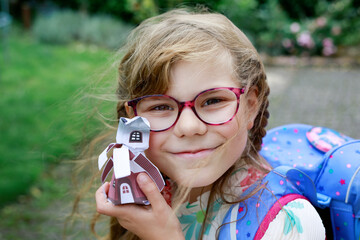 Cute little elementary school girl with eyeglasses and satchel backpack walking outdoors on the way to school. Smiling pupil child ready for back to school, education and childhood lifestyle concept.