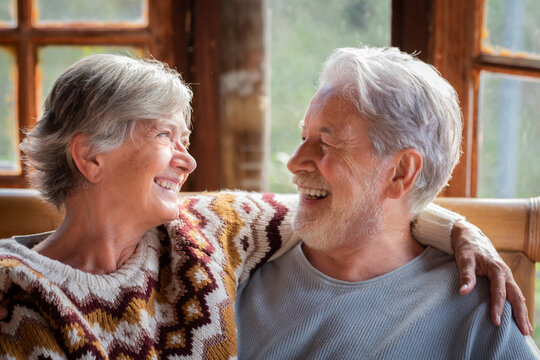 Happy elderly couple spending time together at home in a warm rustic chalet, cuddling, dancing, using laptop or phone, sharing love, joy, and a long-lasting relationship