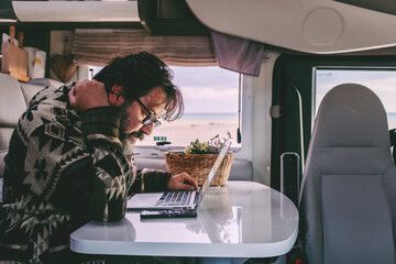 Man working on laptop inside camper van while traveling. Modern digital nomad lifestyle, remote...