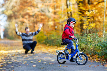 Fototapeta premium Little kid boy and his father in autumn park with a bicycle. Dad teaching his son biking