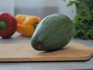 Fresh ripe avocado on the table for making a healthy breakfast or lunch. Avocado on the wooden table with different vegetables on the background