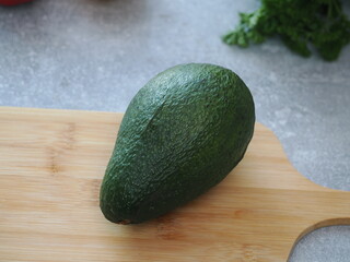 Fresh ripe avocado on the table for making a healthy breakfast or lunch. Avocado on the wooden table with different vegetables on the background