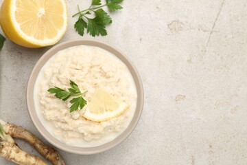 Tasty horseradish sauce with parsley, lemon slice and roots on light table, flat lay. Space for text
