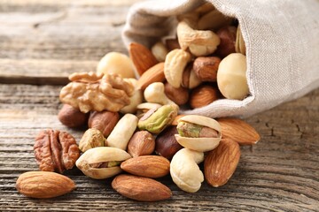 Mix of different nuts in bag on wooden table, closeup