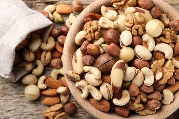 Mix of different nuts in bowl and bag on wooden table, top view