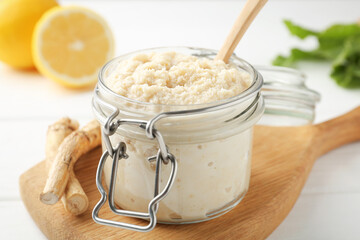 Tasty horseradish sauce, roots and lemons on white wooden table, closeup