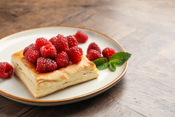 Yummy puff pastry with raspberries on wooden table, closeup