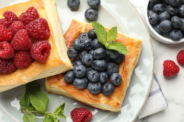 Yummy puff pastries with berries and mint on white table, flat lay