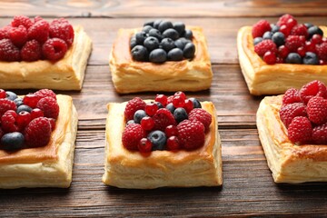 Tasty puff pastries with berries on wooden table, closeup