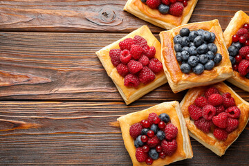 Tasty puff pastries with berries on wooden table, flat lay. Space for text
