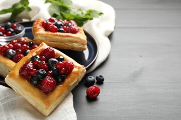 Tasty puff pastries with berries and mint on grey wooden table, closeup. Space for text