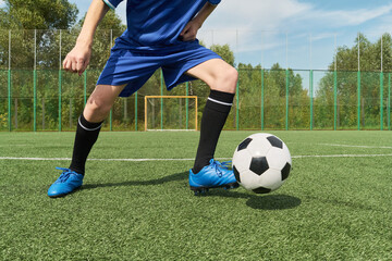 Teenage boy dribbling soccer ball on outdoor field, wearing sports uniform, standing near goal, showing active movement during practice or game, legs and lower body visible