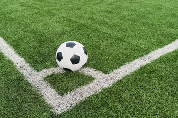 Soccer ball resting on corner of green field near boundary lines, positioned for corner kick, showing close up of sports equipment on outdoor artificial turf