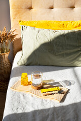 Wooden tray with water glass and vitamin supplement on bedroom bed.