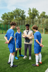 Black man coaching group of teenage boys on outdoor soccer field, holding clipboard and discussing strategy while teenagers listening attentively in sports uniforms
