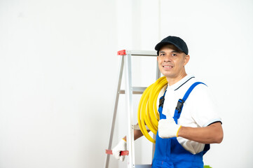 Friendly Technician with Tools: A skilled and confident technician, wearing a cap, coveralls and work gloves, stands proudly beside a ladder, holding a coiled cable.