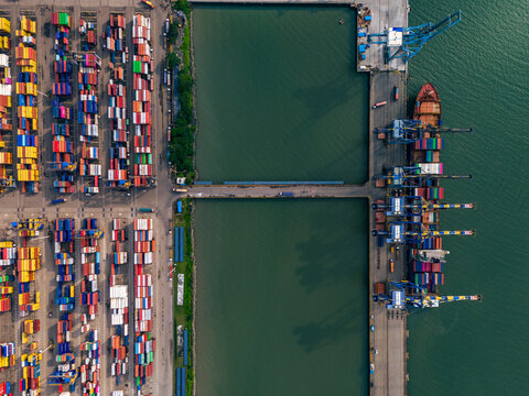 Aerial view of colorful shipping containers stacked in neat rows alongside docks with a docked cargo ship at Jawaharlal Nehru Port Trust (JNPT) in Navi Mumbai, India