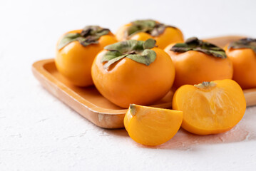 Fresh ripe persimmon on wooden plate with white background, Autumn sweet fruit