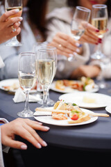 Group of women raising champagne glasses during buffet, with snacks and cheese plates on table.