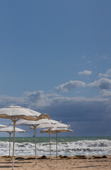 A stormy sea on a sunny day. Grey clouds on the backgrounds and umbrellas in the foreground. 