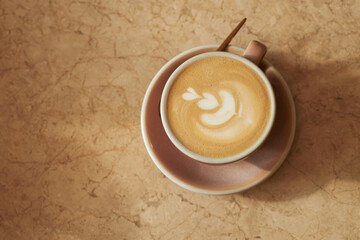 Cup of cappuccino with latte art sitting on marble surface, showing top view of coffee drink in ceramic cup and saucer, wooden stirrer placed on saucer, no people visible