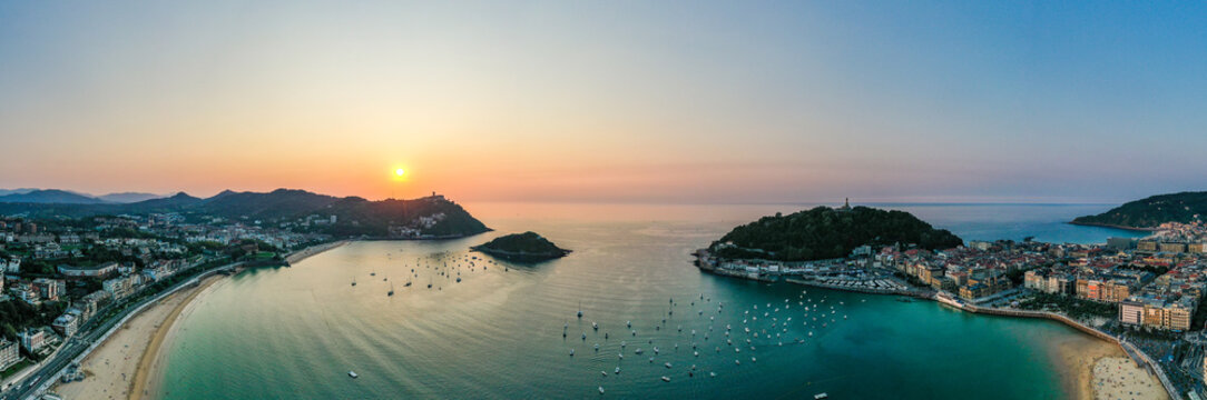 Aerial view of golden light kissing the Playa de la Concha as it meets the vibrant city, the boats dance on the water near Isla de Santa Clara, San Sebastian, Spain.