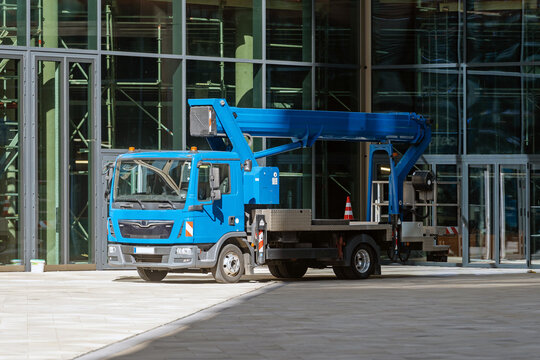 Fototapeta Blue truck-mounted aerial work platform parked in front of a modern glass building