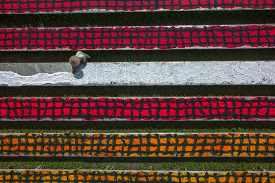 Aerial view of vibrant rows of drying materials create a striking geometric pattern, a person working amidst the colorful display, Mojolaban, Central Java, Indonesia.