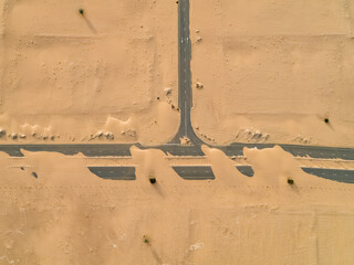 Aerial view of roads cutting through the undulating desert landscape, the fine sand creating fluid patterns around the stark asphalt, Dubai, Dubai, United Arab Emirates.