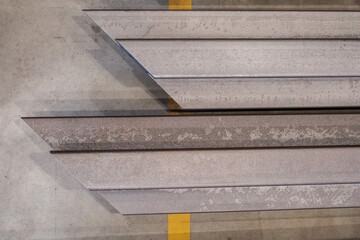 Stacked structural steel profiles in warehouse, close-up of industrial metal beams with worn texture and shadows on concrete floor