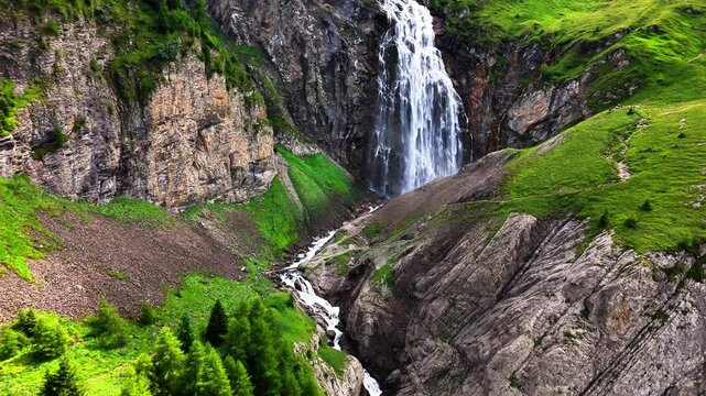 Engstligenf&auml;lle near Adelboden in Switzerland cascades from rugged alpine cliffs into a lush valley, surrounded by steep slopes, forested ridges, open meadows, and distant peaks capped with snow
