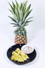 Sliced Pineapple on a Black Plate with Dipping Sauce and a Whole Pineapple, White Background