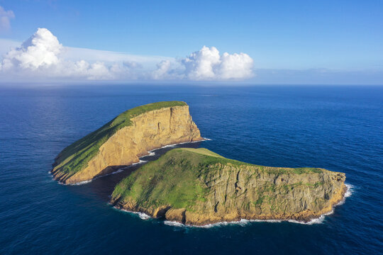 Aerial view of the stark cliffs of Ilheus das Cabras rise majestically from the azure waters, a verdant jewel amidst the vast ocean expanse, Port Judeu, Azores, Portugal.