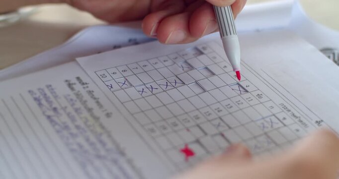 Teacher marking student exam papers with a red pen using a prepared answer sheet template.