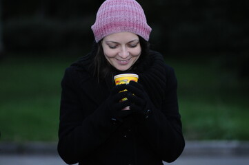 A girl in a black coat and hat is drinking a hot drink.