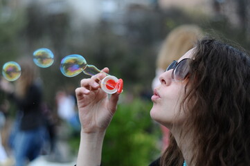 A girl with curly hair blows soap bubbles