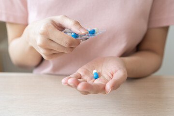 Sick ill asian young woman, girl hand taking tablet pill capsule out from blister pack, painkiller medicine from stomach pain, head ache, pain for treatment, take drug or vitamin at home, health care.