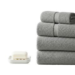 Neatly folded stack of three plush dove grey terry cloth bath towels, white ceramic soap dish with soap on a light grey background, concept of luxurious bath essentials